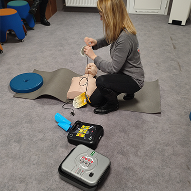 Photo d'une personne installée proche d'un mannequin effectuant une démonstration de massage cardiaque.